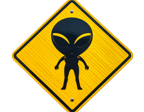 A yellow diamond road sign displays an alien silhouette with large eyes. The sign has a textured, reflective surface