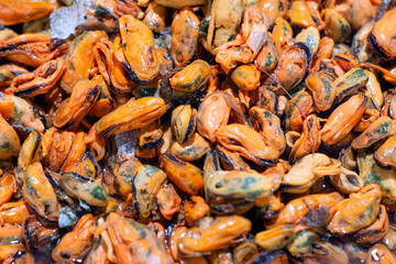 Close-up of fresh orange mussel meat displayed on ice at a seafood market