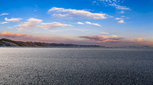Empty asphalt road with distant mountain landscape and wind turbines under a beautiful sunset sky