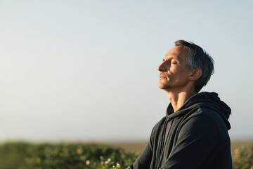man sits peacefully with his eyes closed meditating in serene environment