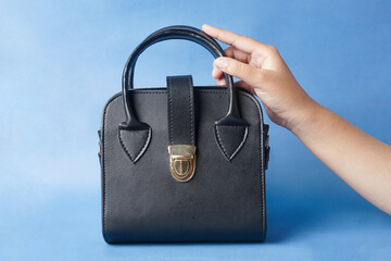 A black bag sits on a hand against a striking blue background