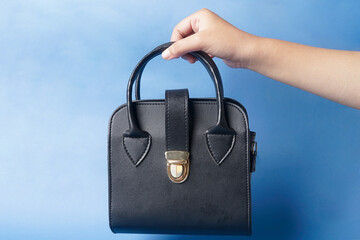 A black bag is held by hand on a bright blue background