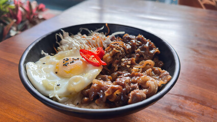 Bowl of Asian Beef and Egg Rice Dish with Vegetables in Black Bowl on Wooden Table