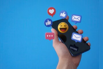 Hand holding a smartphone with social media icons and laughing emoji