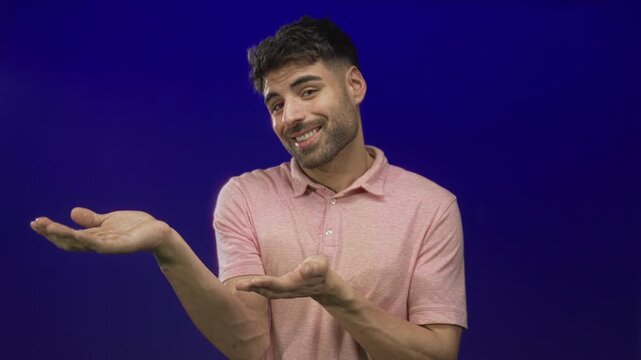 Young hispanic man wearing pink polo shirt with open hands presenting and smiling in studio; confidence.