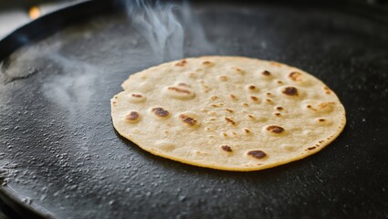 A round flatbread is cooking on a hot griddle, with steam rising from its surface, showcasing the golden-brown spots and texture, creating an inviting culinary atmosphere