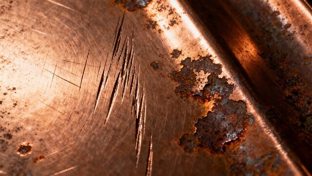 Extreme close-up of a damaged copper surface featuring deep scratches and rough patches of dark rust, creating a weathered industrial texture.
