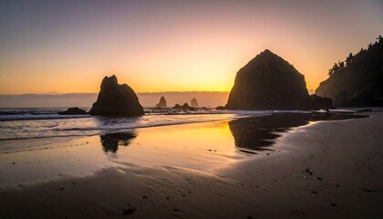 A coastal sunset casts a golden glow on the beach and sea stacks, with the sun's reflection mirrored in the wet sand