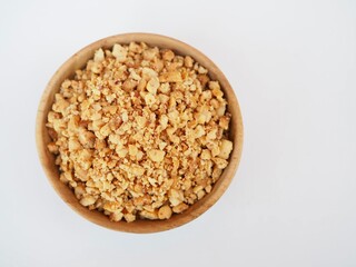Crushend peanuts in  a wooden cup placed on a white background.