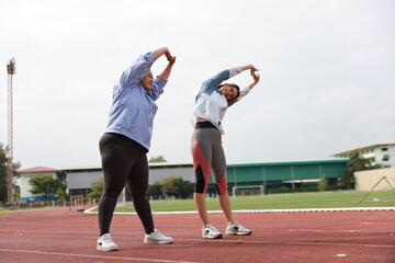 Two slim and plus size woman with sport jacket together stretch warm-up exercise on an outdoor running track, wellness and healthy lifestyle