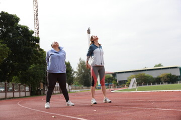 Two slim and plus size woman with sport jacket together stretch warm-up exercise on an outdoor running track, wellness and healthy lifestyle