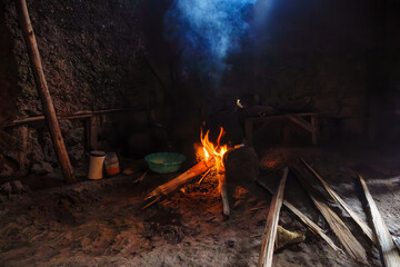Cooking fire blazing smoking inside African villagers hut by wooden table and basic furniture in Gasure Rwanda.