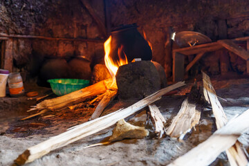 Cooking fire blazing inside villagers hut by wooden table and basic furniture