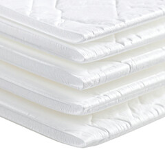 Stack of white, quilted mattress toppers, angled view