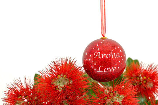 A red Christmas bauble seen against a white background with the striking red flowers of New Zealand's Summer flowering Pohutukawa tree. The tree is known as the NZ Christmas tree.