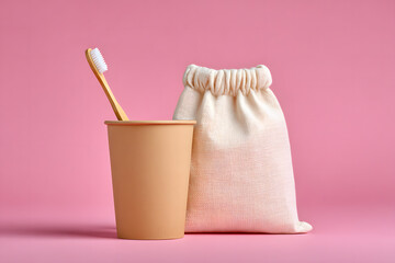 A sustainable bamboo toothbrush with a canvas bag and paper cup against a pink backdrop, promoting eco-friendly habits