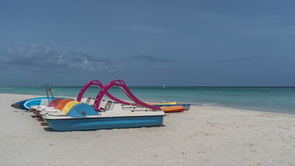 A row of colorful tourist boats, catamarans and canoes on a sandy beach by the sea. Calm turquoise ocean, white sand, blue sky. Cuba. Varadero. Resort. Copy space