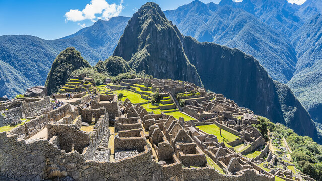 View from the height of the famous Lost City of the Incas Machu Picchu. Dilapidated stone walls of buildings, green terraces on the mountainside. Huayna Picchu and the mountain range against the sky. 