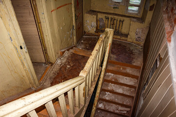 Haunting abandoned building interior with a dilapidated wooden staircase. Peeling paint and grimy debris on steps show urban decay, historical neglect, and forgotten architecture