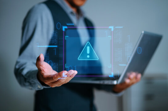A professional man holding a laptop with a digital warning alert floating above his hands, symbolizing system error, cyber risk, and critical digital malfunction.