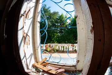 Sunlit, decaying window frame of an abandoned early 20th-century mansion reveals an overgrown summer yard