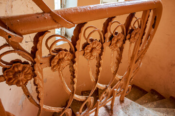 Detailed close-up of an old, ornate metal banister with peeling paint and cobwebs, part of a decaying staircase in a forgotten early 20th-century mansion