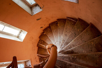 Gritty, worn spiral staircase descends within a forgotten early 20th-century abandoned manor, bathed in faint light