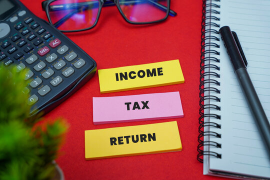 Colorful sticky notes with word 'Income Tax Return' with calculator and glasses on a red table for financial planning concepts.