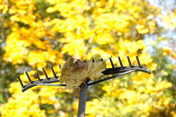 Autumn leaves rest on a rake against a backdrop of vibrant yellow foliage