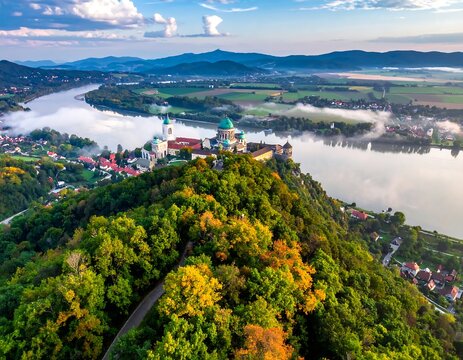 Aerial view captures a hilltop church, river, and landscape, shrouded in mist, with vibrant foliage and rolling hills