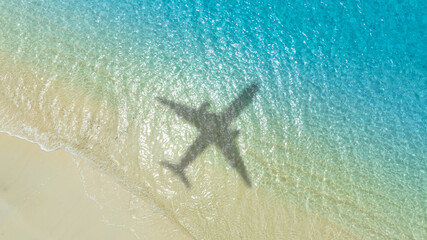 Naklejka premium Aerial view of shadow passenger plane silhouette and sandy beach blue sea with waves at sea beach summer vacation sea travel concept 