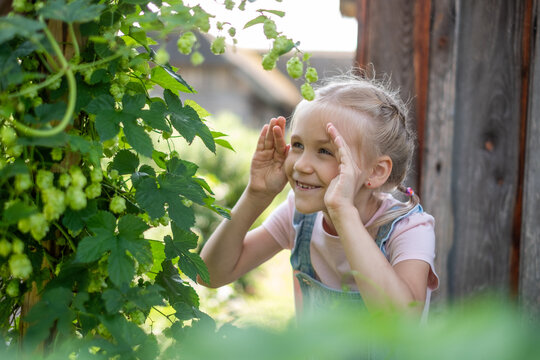 Young girl joyfully playing outdoors in a lush garden, surrounded by green plants and flowers, capturing the essence of summer fun and childhood exploration
