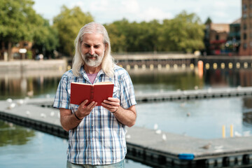 Senior man enjoying a book by the canal in london