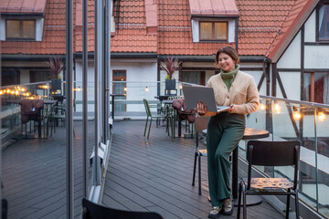 Middle-aged woman working remotely on a laptop in a cozy food court, surrounded by warm lighting and modern decor, enjoying a productive atmosphere with copy space