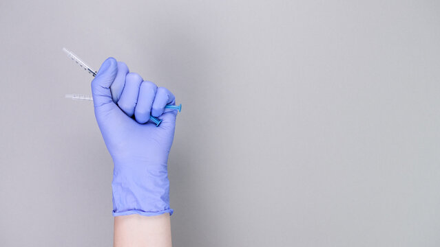 Hand in blue gloves of doctor or nurse holding syringe with liquid vaccine over grey background with copy space. New vaccine. Unknown vaccine. Medical gloves.