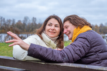 Midlife couple enjoying a cozy autumn day, sitting on a bench by the lake, sharing laughter and warmth, surrounded by colorful fall foliage and a serene atmosphere