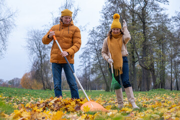 Midlife couple raking colorful autumn leaves in a park, wearing cozy sweaters and hats, enjoying the fall season together while creating a vibrant outdoor atmosphere