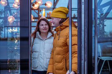 Midlife couple enjoying a cozy evening in a stylish cafe, illuminated by warm lights, sharing smiles and laughter, creating a romantic atmosphere together