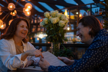 Midlife couple enjoying a delightful evening at a cafe, sharing laughter and conversation over a menu, surrounded by warm lighting and beautiful floral arrangements