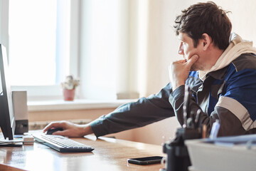 A focused man sitting at a desk, working on a computer in a bright office. The setting conveys productivity and concentration.