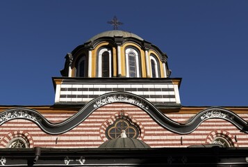 Close view of the honey-colored dome of the Rila Monastery chapel, showing the cross on top, the inscription “1870,” and the colorful arches and columns, Rila, Bulgaria, 01 Nov. 2025