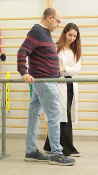 Physiotherapist assisting a man walking with parallel bars