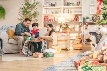 Asian family enjoying holiday together, parents and son wrapping Christmas presents in warm home atmosphere, smiling while creating gifts and decorations, symbol of love, unity, and togetherness.