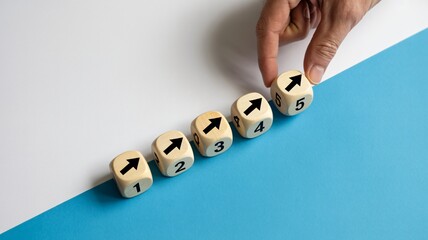 Hand guides wooden dice showing ascending numbers and upward arrows, symbolizing growth and progress in business strategy