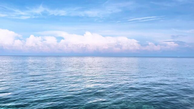 Calming ocean waves gently rolling under a bright blue sky with fluffy white clouds, a peaceful scene in 4k 60 fps