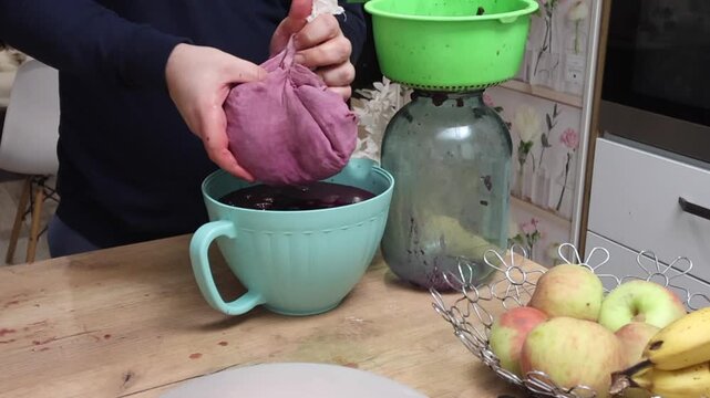 A man strains fermented grapes, squeezing the fermented berries through cheesecloth to make homemade wine