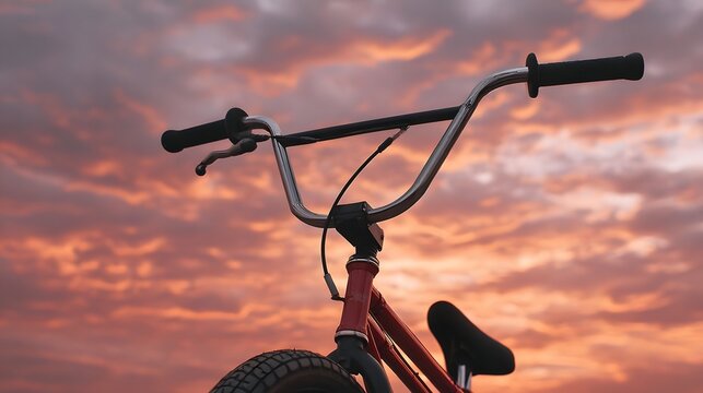 A close up of a BMX bicycle s handlebars against a vibrant cloudy sunset sky