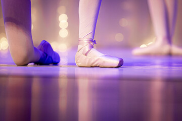 Naklejka premium Close-up focado nos pés de uma bailarina usando sapatilha de ponta rosa-claro com fitas de cetim. A imagem é capturada de um ângulo baixo no palco de um teatro. Outras dançarinas estão no fundo, suave