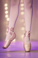 Close-up vertical e de corpo inteiro das pernas de uma bailarina em palco, exibindo a posição correta dos pés na sapatilha de ponta rosa-claro. As sapatilhas de cetim e as meias-calças estão envoltas  © warleysoares