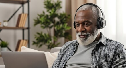 Senior Man Enjoying Music or Online Content with Headphones and Laptop in a Cozy Home Setting Radiat.jpg
